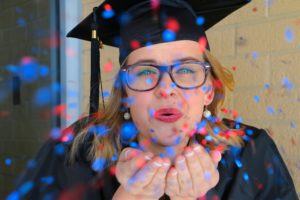 Graduation Celebration: High school graduate wearing graduation cap blowing red and blue confetti.