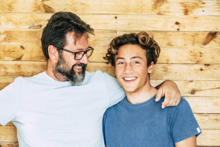 Father and son portrait - adult and young teenager generations smile and hug together